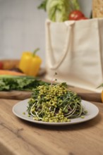 A fresh topped with green sprouts on a white plate sits on a wooden table. In the background,
