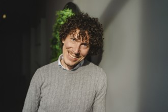 A young man with curly hair stands in front of a green wall, symbolizing themes of ecology and