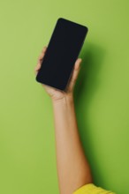 Crop hand of anonymous person holding smartphone with black screen against green background