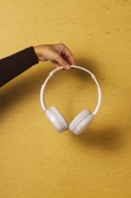 Crop hand holding headphones on golden background