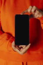 Crop anonymous female in orange casual clothes showing smartphone with empty screen