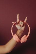 Crop anonymous woman holding headphones and making the rock sign over dark red background