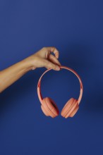 Crop anonymous person holding wireless pink headphones over blue background