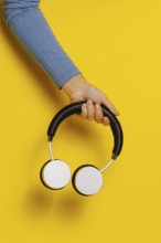 Crop hand holding headphones on yellow background