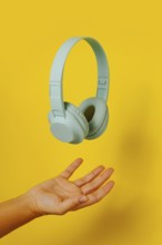 Crop anonymous person holding levitating headphones on yellow background