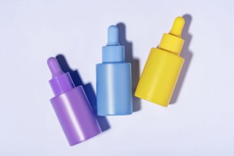 Top view of three vibrant-colored cosmetic serum bottles in purple, blue, and yellow neatly