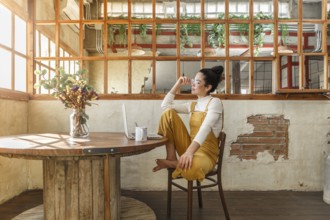 A young woman enjoys a coffee break in a sunlit rustic loft, with a laptop nearby, illustrating a