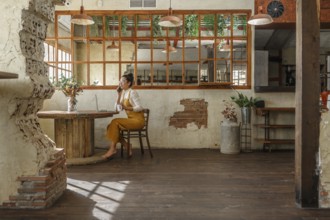 A woman teleworking in a vintage style cafe, using a laptop and smartphone as she engages in a