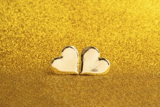 Two golden heart-shaped objects set against a shimmering golden backdrop, ideal for St. Valentine's