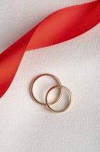 Top view of two golden wedding rings lying on a textured white fabric, intertwined with a vibrant