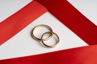 Two gold wedding rings lie elegantly on a vibrant red satin ribbon, symbolizing romance and