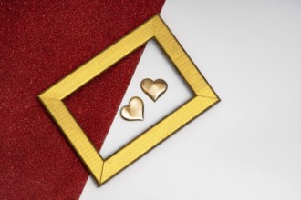 Two golden heart-shaped objects and a rectangular golden frame on a red glittery background,