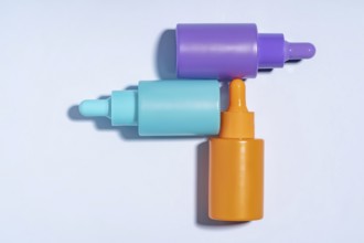 Top view of three vibrant serum bottles in purple, turquoise, and orange colors, designed with