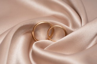 Two golden wedding rings interlocked, symbolizing unity and love, rest gently on a luxurious satin