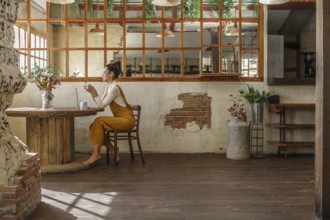 A woman engages in teleworking using a laptop at a circular wooden table in a rustic, beautifully