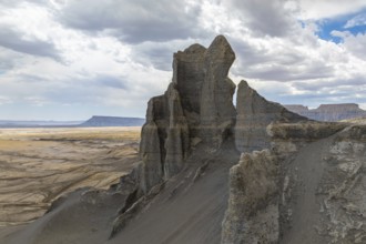 A towering rock formation emerges from the expansive desert landscape under a cloudy sky in