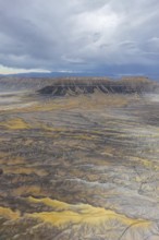 Aerial view of a rugged desert landscape featuring mesas under a cloudy sky in Hanskville, Utah.