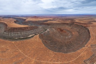 An aerial view showcases a river elegantly meandering through layered rock formations in a vast San