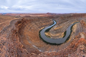 Aerial view of a winding river carving through layers of ancient rock formations in a desert San