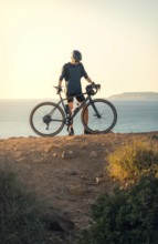 Male cyclist holding his road bike and gazing at the sea during sunset in Zahara de los Atunes,