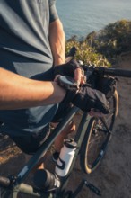 Cropped unrecognizable male cyclist leaning on his bicycle, looking at his watch, with a scenic