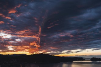 Breathtaking view of vibrant sunset skies above rolling hills framing a serene coastal backdrop,