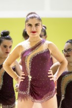 A confident gymnastic whit disability in a burgundy outfit adorned with rhinestones stands onstage