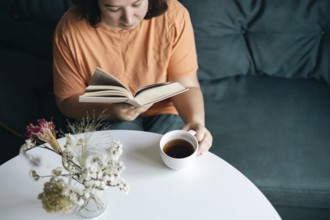 Focused woman reading a book and sipping coffee at a round white table, with a relaxed atmosphere