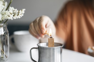 Cropped unrecognizable woman lights a candle placed in a metal mug, creating a cozy atmosphere at