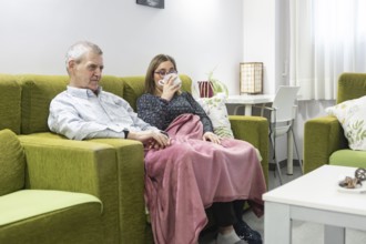 A couple with intellectual disabilities sit comfortably on a green sofa wrapped in a pink blanket.