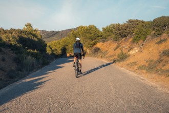 Back view of an unrecognizable male cyclist riding on a quiet road through the hills near Faro