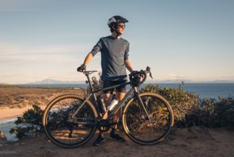 A male cyclist stands with his bike, overlooking the scenic Zahara de los Atunes, Cadiz during a