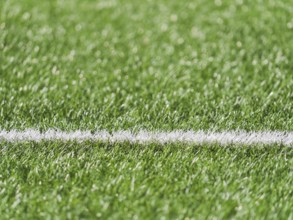A close up image showcasing the lush green grass of a soccer field with a crisp white line marking.