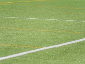 A close up view of a green artificial turf soccer field, featuring vibrant white and yellow lines