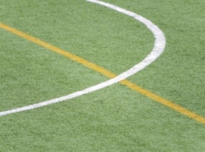 A close up of white and yellow lines marking a soccer field on artificial green turf. The detailed