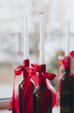 Elegant Valentine's Day decor featuring white tapered candles in wine bottles adorned with red