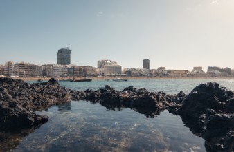 Tranquil cityscape view from volcanic rocks on a sunny day, showing modern buildings and calm