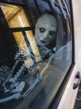 A haunting skeleton figure peers through a city window, its eerie reflection captured on the glass.