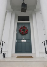 A stylish London doorway features a festive wreath with red ornaments, pinecones, and greenery