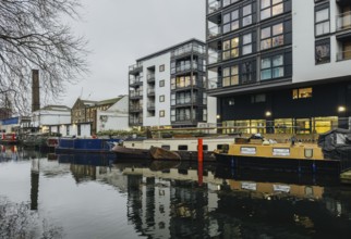 A serene London canal scene showcasing modern apartments alongside moored boats. The calm water