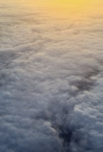 Captured from above, this image showcases a stunning blanket of fluffy clouds illuminated by a warm