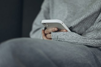A person in a soft gray sweater holds a smartphone, reflecting a comfortable and relaxed moment.