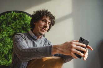 A curly-haired young man, sitting against a vivid green wall, emphasizes themes of ecology and
