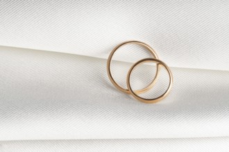 A pair of golden wedding rings overlap on a soft textured fabric, symbolizing love and commitment
