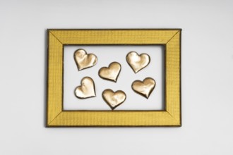 A collection of golden heart shapes arranged inside a textured gold frame, evoking themes of love