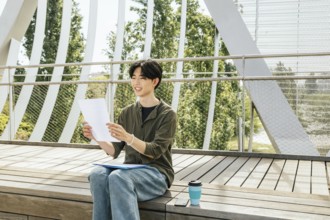 A young man study outside on wooden steps. The student smiling and reading notes. The atmosphere is