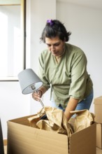 A trans woman is unpacking a lamp from a cardboard box in her new home, symbolizing fresh starts
