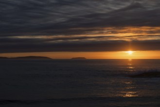 A serene sunset over the ocean, with the sun casting radiant orange and yellow hues across the sky.