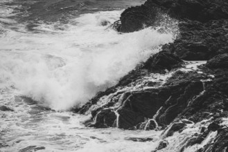 A dynamic black and white photograph capturing the power and drama of waves crashing against rugged
