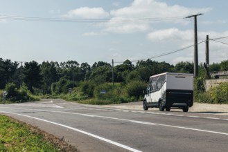 A motorhome drives on a serene rural road surrounded by lush greenery and power lines under a clear